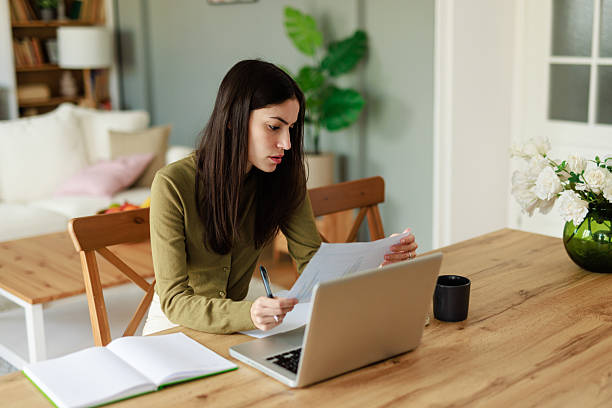 istock Focused Young Woman in Olive Sweater Reviewing Documents at Home Workspace in Bright Lighting 2223829491