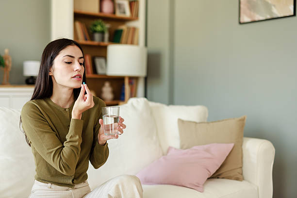 istock Young Woman Taking Daily Medication While Relaxing On Comfortable Couch In Living Room Setting 2223829601