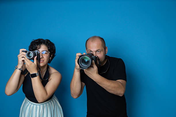 A female and a male photographer taking photos with professional cameras in a studio setting with a vibrant blue background