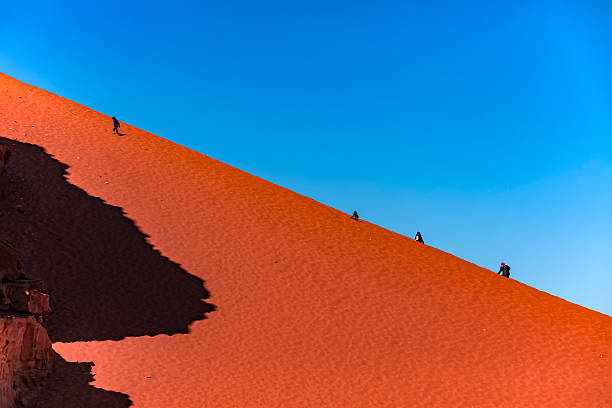 Tourists Walking on Red Sand Dune in Wadi Rum stock photo