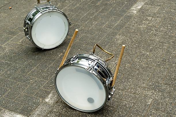 Two snare drums and drumsticks lying on a cobblestone street, ready for a street musician or a marching band performance