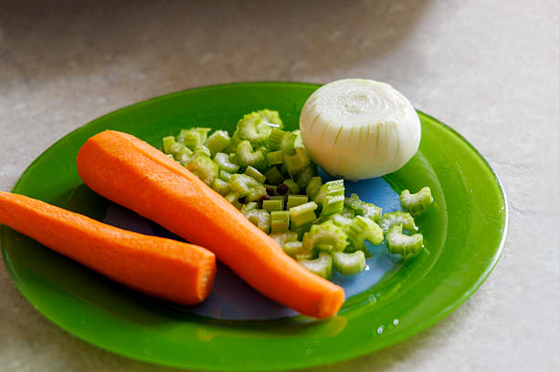 Fresh vegetables are displayed on a green plate, including two peeled carrots, chopped celery stalks, and half an onion.