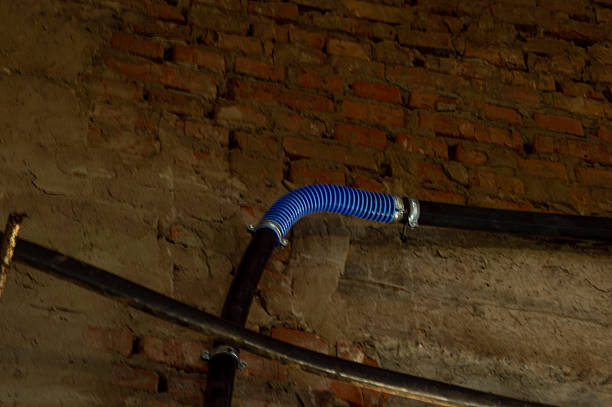 Exposed brick wall features a blue flexible ducting alongside dark pipes in a dimly lit industrial environment.