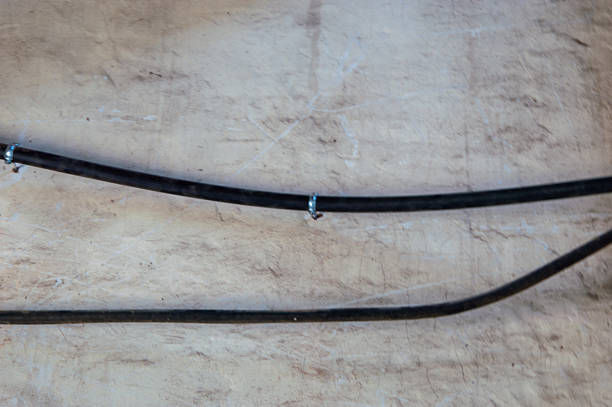 Two black rubber hoses are neatly arranged with metal clamps, resting on a light-colored surface in a workshop environment.