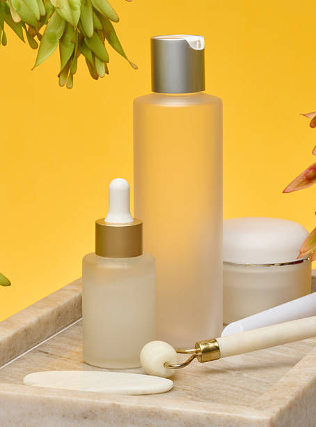 Various cosmetic bottles pipette, spray, jar, roller massager and guasha on a marble stand.