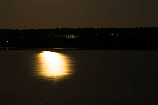 A body of water with a bright light reflecting on it. Water. Outdoor. Sky. River. Sunset