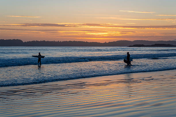 Surfers with surfboards on Chesterman beach at sunset, Tofino, Vancouver Island, British Columbia, Canada.