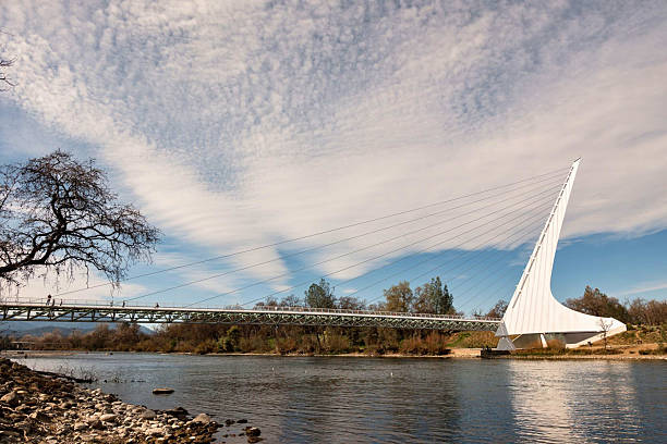 Redding, California, United States  November 7 2024: A side view of the Sundial Bridge reflects in the river beneath streaked clouds and autumn trees. Editorial use only.