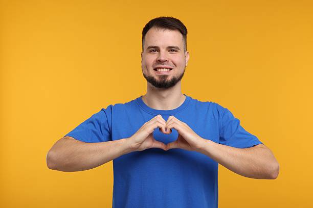 istock Man showing heart gesture with hands on golden background 2223877056