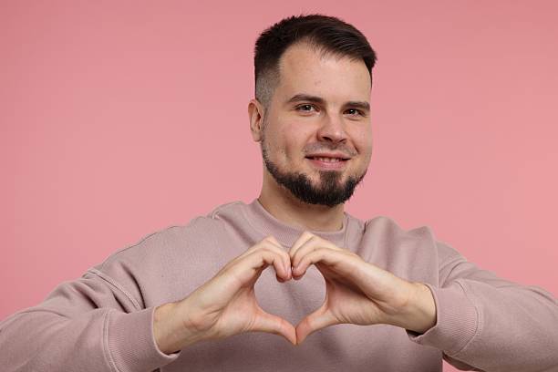 istock Man showing heart gesture with hands on pink background 2223877062
