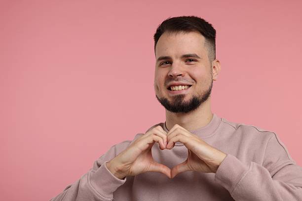 istock Man showing heart gesture with hands on pink background 2223877073