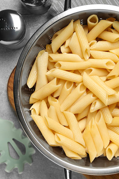 istock Delicious penne pasta in colander, spices and spoon on gray table, flat lay 2223877656
