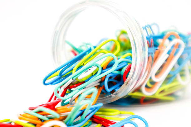 Colorful paper clips spilling from a glass jar on a white background