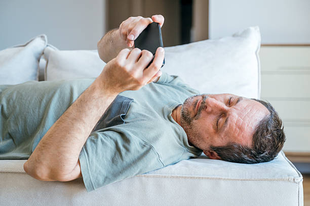 istock Lazy couch potato guy using mobile phone while laying on living room sofa 2223882085