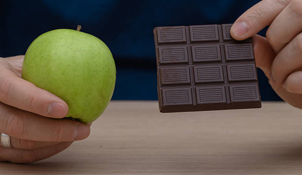Photograph of an apple and a bitten chocolate bar with contrasting colors on a white background