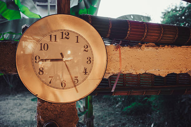 Old clock on a concrete pillar in the balcony, close-up view, yard in the background in the early evening.