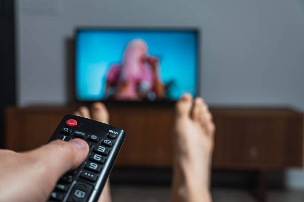 istock Person relaxing on couch watching television and changing channels 2223889536