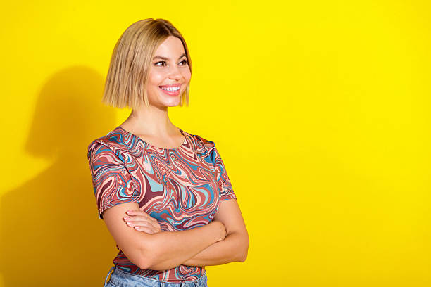 istock Young woman with smiling expression wearing trendy patterned top against a vibrant yellow background in studio setting 2223891539
