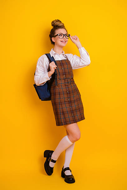 istock Young female student wearing formal school uniform with stylish glasses posing against a bright yellow vertical background 2223891762
