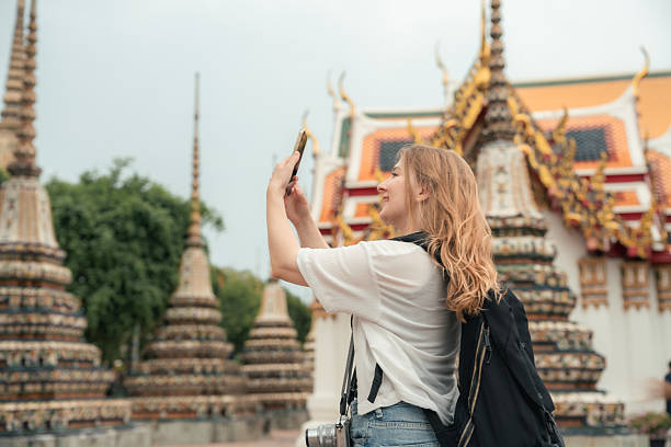 istock Young female tourist using her smartphone to take selfies with Buddha statues inside a serene temple 2223896476