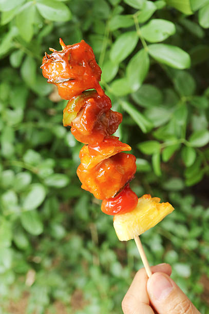 Hand Holding a Mouthwatering Charcoal Grilled Barbecues on Green Foliage Backdrop