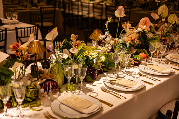 A beautifully arranged long dining table is set for a luxurious wedding dinner, featuring floral centerpieces, fine glassware, gold cutlery, and a romantic ambiance