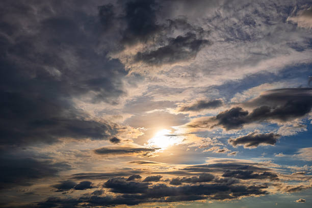 Dramatic sky background at sunset with sun shining through incoming stormy clouds.