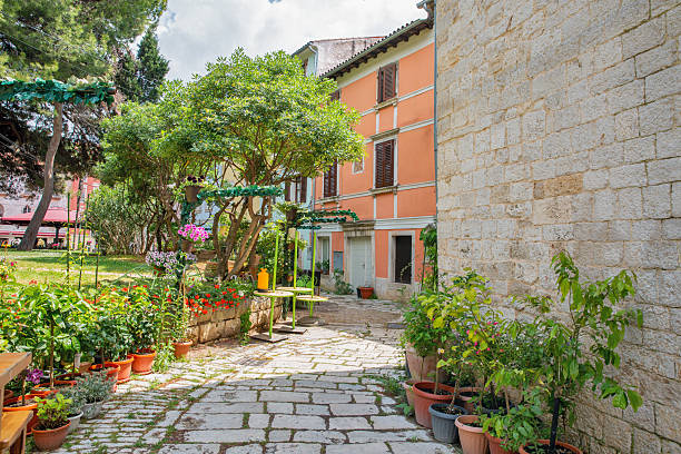 Quiet courtyard with potted plants and blooming flowers beside colorful old buildings in the historic center of Porec, Croatia. Peaceful summer garden scene.