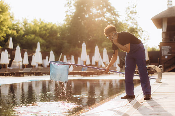 istock Pool cleaner is using landing net and talking on the phone during his work at luxury resort 2223907659