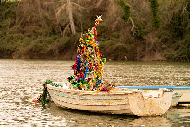 Small fishing boat adorned with a vibrant christmas tree, floating gracefully on the pisuerga river in spain, creates a festive and unique winter scene full of holiday spirit