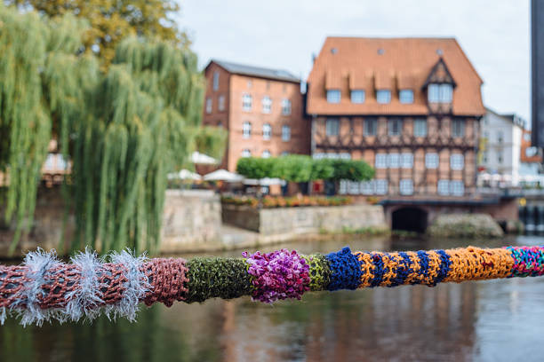 Colorful yarn bombing decorates a bridge railing with traditional buildings in the background, Lüneburg, Germany
