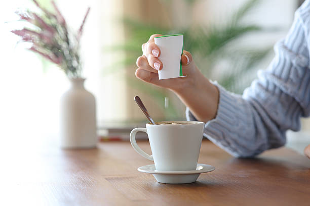 Woman hand throwing saccharin pill on coffee cup at home stock photo