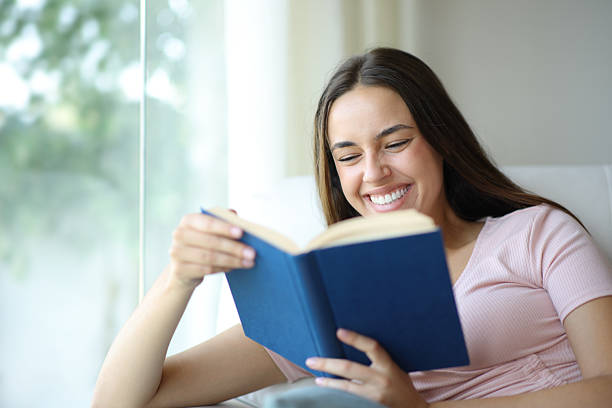 istock Happy woman is reading a paper book on a sofa 2223912481