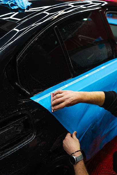 istock Detailing expert uses red squeegee wrapper to flatten blue PPF wrap on car surface. Vehicle wrap detailing involves squeegee strokes for seamless, wrinkle-free adhesion. 2223914384