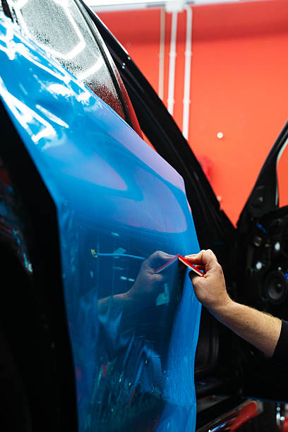 istock Detailing expert uses red squeegee wrapper to flatten blue PPF wrap on car surface. Vehicle wrap detailing involves squeegee strokes for seamless, wrinkle-free adhesion. 2223914397