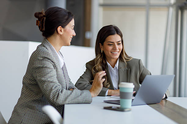 istock Professional women collaborating, sharing laptop screen, working harmoniously in contemporary workspace 2223914487