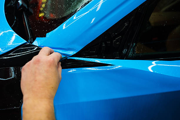 istock Detailing technician trims blue PPF on a car panel for perfect contour fit. Cutting blue PPF with blade. Cutting blue paint protection film with blade during detailing job ensures precision edges. 2223915187