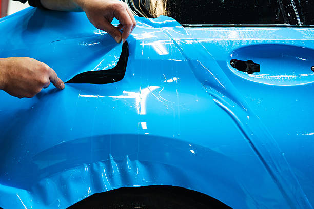 istock Detailing technician trims blue PPF on a car panel for perfect contour fit. Cutting blue PPF with blade. Cutting blue paint protection film with blade during detailing job ensures precision edges. 2223915262