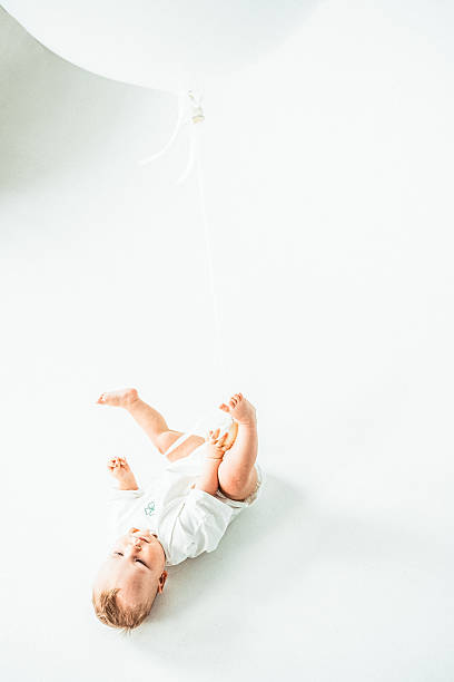 istock Baby lying on white floor holding balloon with joyful expression and playful pose. 2223915595