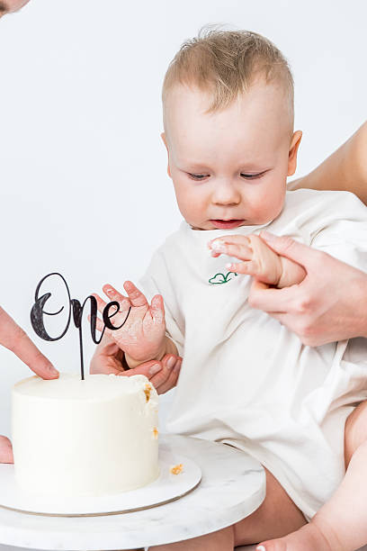 istock Baby celebrating first birthday with white cake and helping hands around it. 2223915762