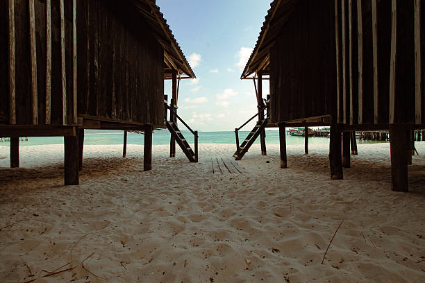 Wooden huts on a sandy beach overlooking a calm ocean under a blue sky in Koh Rong Sanloem, Sihanoukville, Cambodia that shows the candid local daily island life