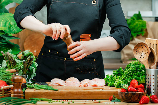 Chef effortlessly seasons fresh chicken with herbs and spices while surrounded by vibrant vegetables in a warm, inviting kitchen.