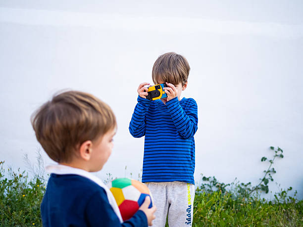 Children playing outdoors while one captures moments with a disposable camera in a sunny field