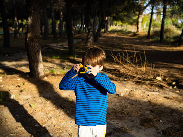 istock Young boy taking pictures with a disposable camera in a forest during a sunny afternoon 2223921009