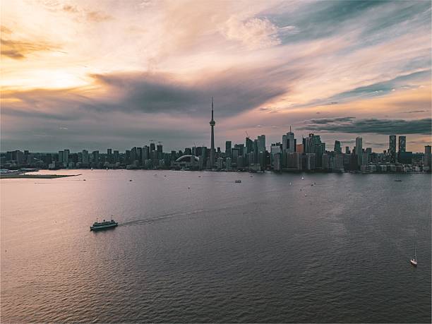 A stunning view of Toronto's skyline at sunset with a ferry on Lake Ontario and dramatic clouds overhead.