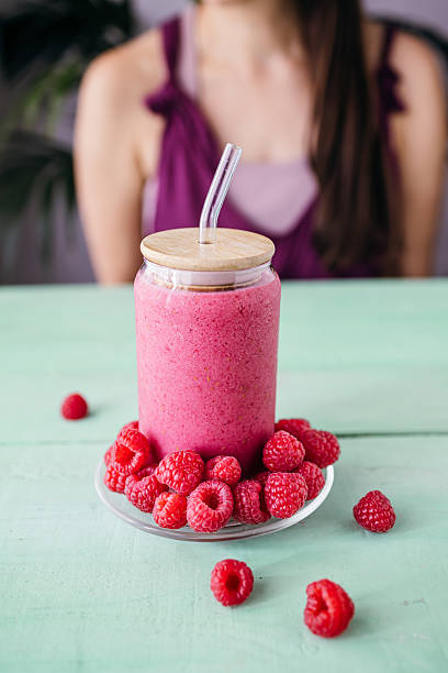 A vibrant raspberry smoothie placed in the foreground with a woman visible in the background.