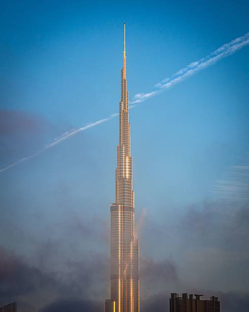 Dubai, United Arab Emirates – February 17, 2023: The Burj Khalifa in Dubai stands tall against a clear blue sky with a contrail crossing the scene, capturing its architectural magnificence.