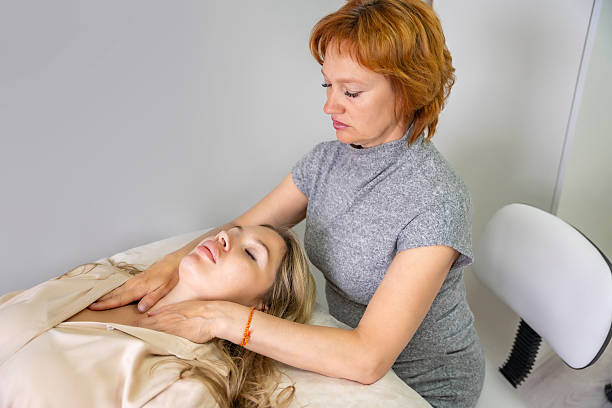 istock Female practitioner performs facial lifting technique on a young woman lying on a couch. Concept of energy healing, face therapy and alternative wellness practice from Access Bars. 2223927029