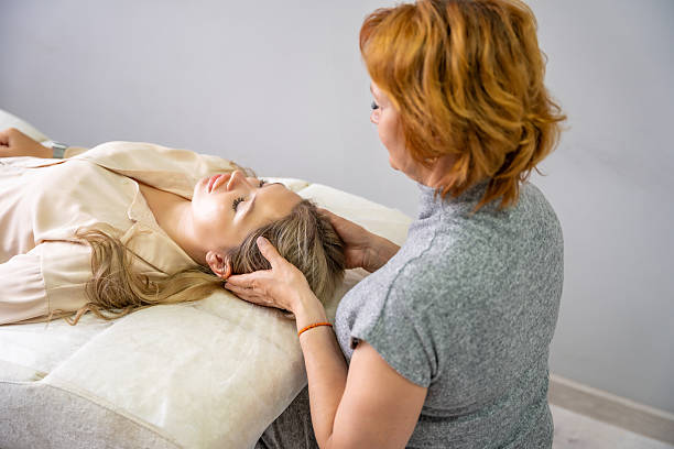 istock Female practitioner performs facial lifting technique on a young woman lying on a couch. Concept of energy healing, face therapy and alternative wellness practice from Access Bars. 2223927063