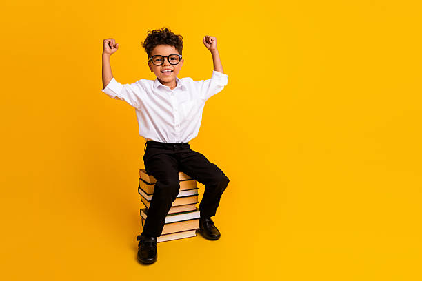 An adorable preschool age little boy smiles for the camera as he stands in his preschool classroom and waive to the camera.